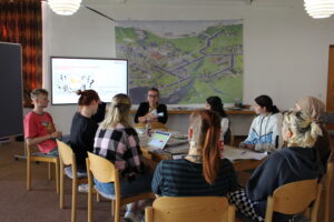 Junge Menschen sitzen mit Moderation des Workshops zusammen um einen Tisch bei der #MitmischenNRW-Konferenz im Juni 2023 in Wuppertal