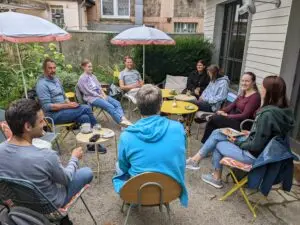 Die Teilnehmenden des Klimapsychologischen Workshops tauschen sich draußen in lockerer Runde aus. Sie sitzen auf Gartenstühlen, essen Waffeln und trinken Kaffee.